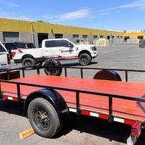 A red trailer is parked next to a white truck in a parking lot.