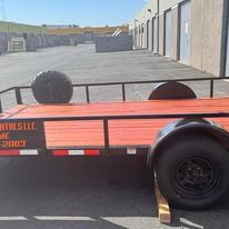 A red trailer is parked in a parking lot next to a building.