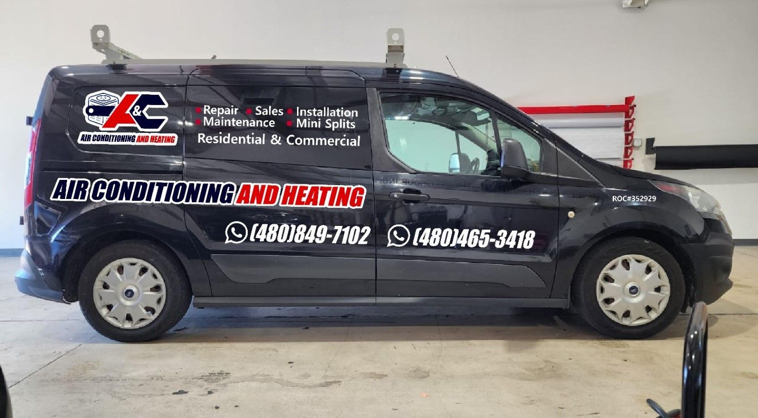 A black van with the words air conditioning and heating on the side is parked in a garage.