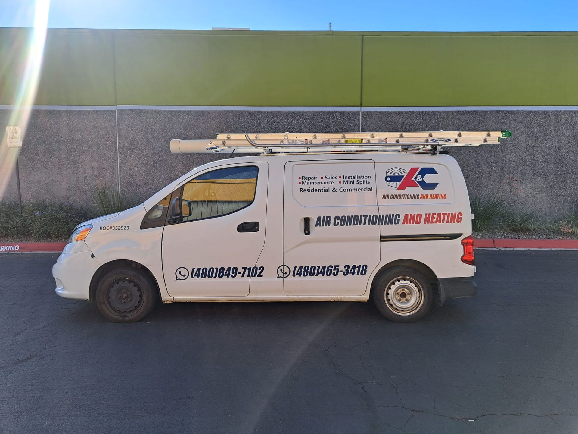 A white van with a ladder on top of it is parked on the side of the road.