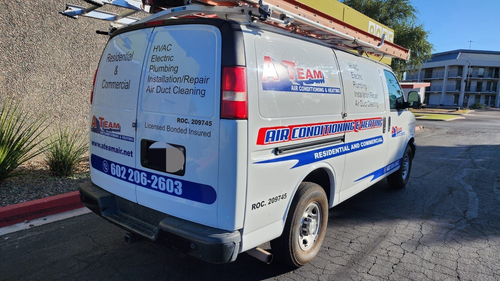 A white van with a ladder on top of it is parked in a parking lot.