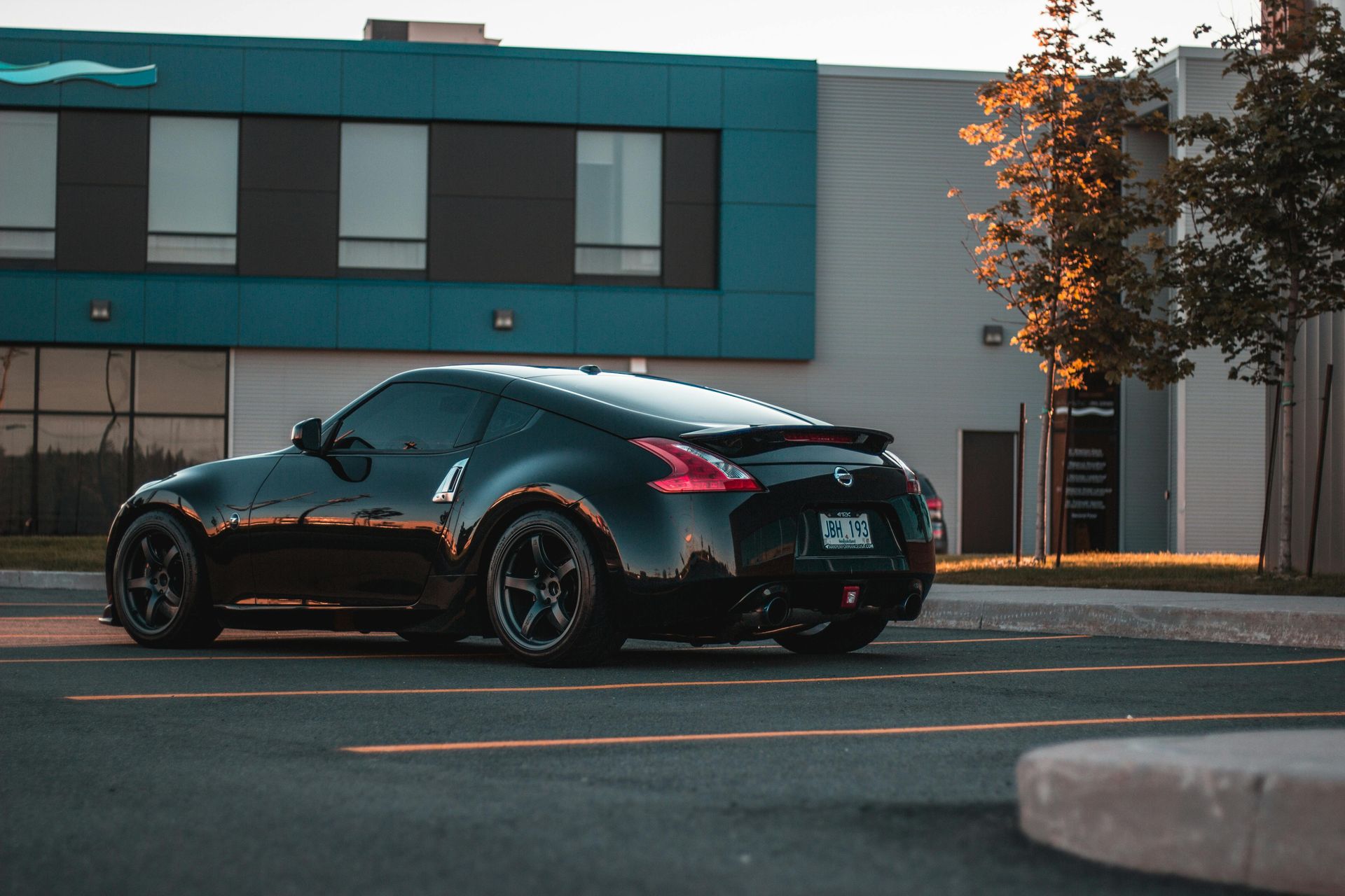 A black sports car is parked in a parking lot in front of a building.