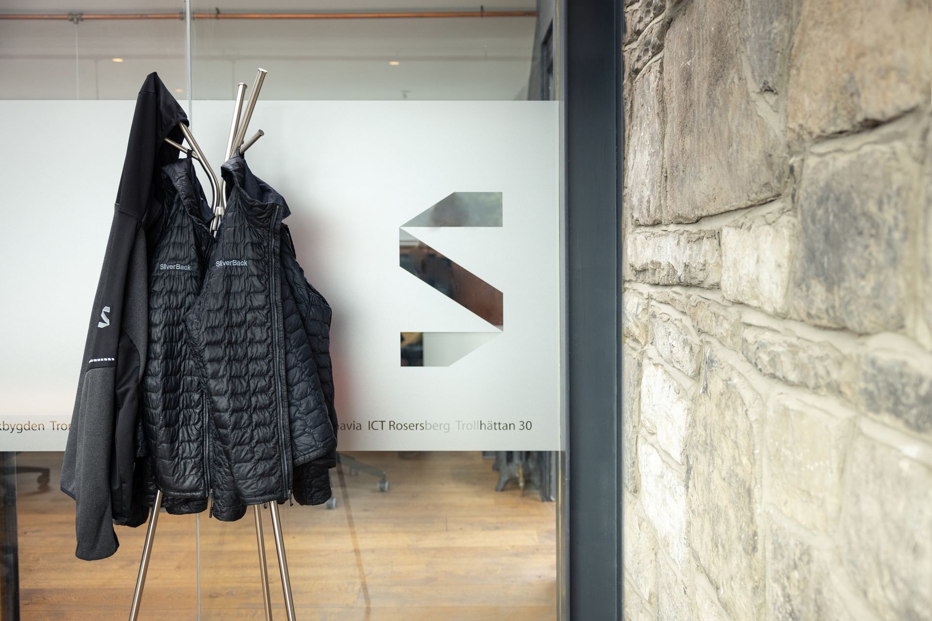 A black jacket is hanging on a coat rack in front of a glass door.