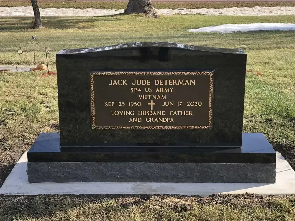 Black granite gravestone with gold lettering on a gray base in a grassy cemetery.