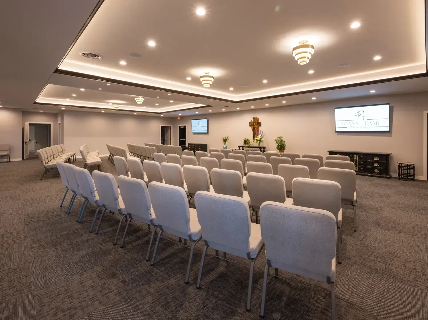 Empty conference room with rows of white chairs, ceiling lights, and wall-mounted screens