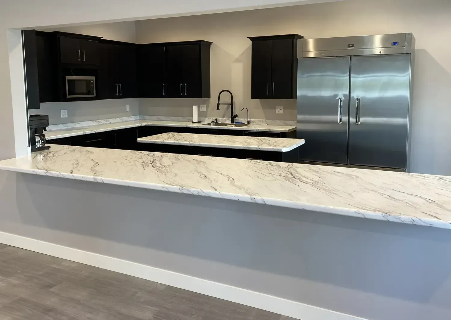 Modern kitchen with black cabinets, white marble island, stainless steel fridge, and faucet sink