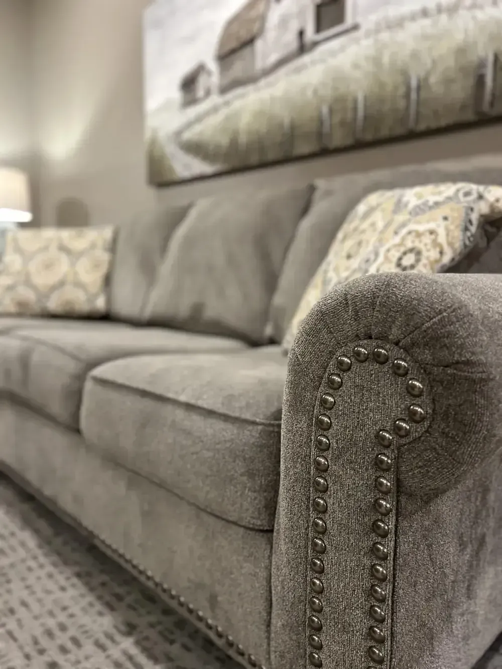 Gray upholstered sofa with nailhead trim and patterned pillows in a living room