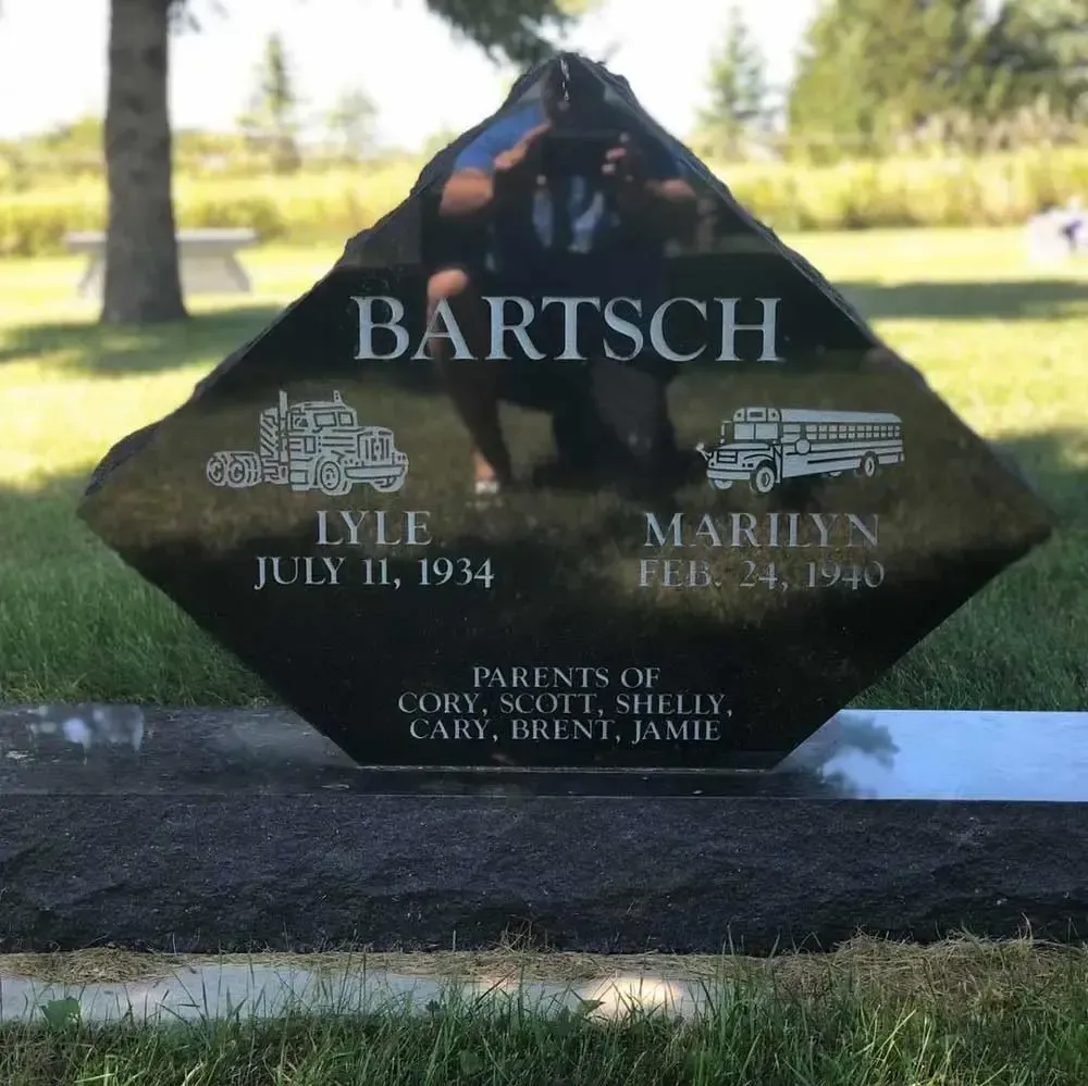 Black BARTSCH family gravestone with engraved portraits and names in a sunny cemetery
