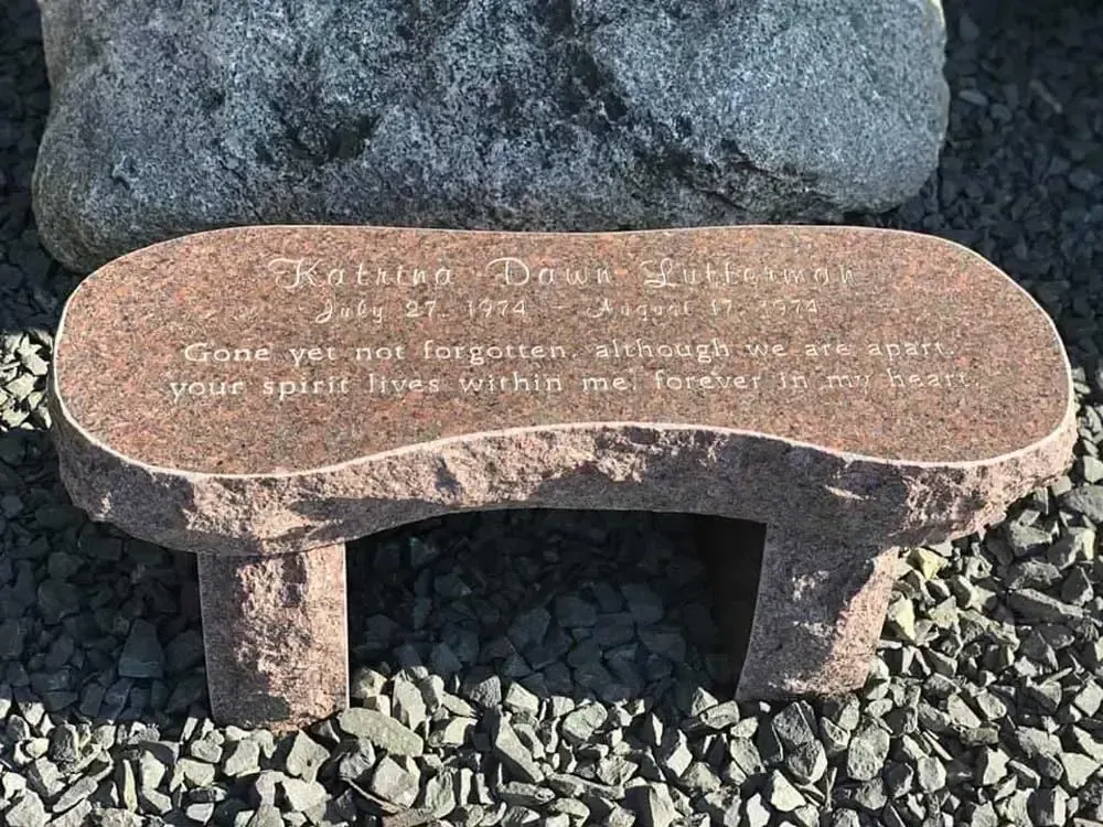 Brown memorial bench with engraved text on gravel in front of rocks