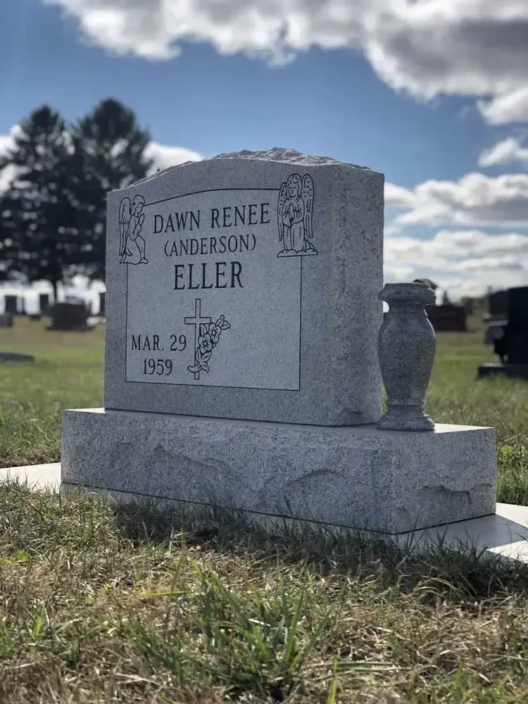 Gravestone in a cemetery under a cloudy blue sky, with trees in the background.