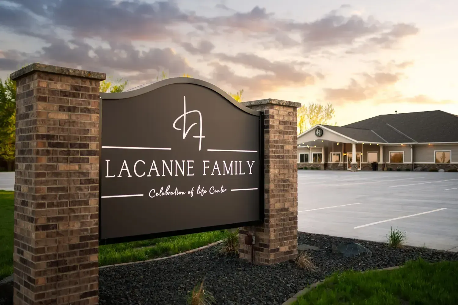 Lacanne Family sign at a brick entrance, with a building and empty parking lot at sunset