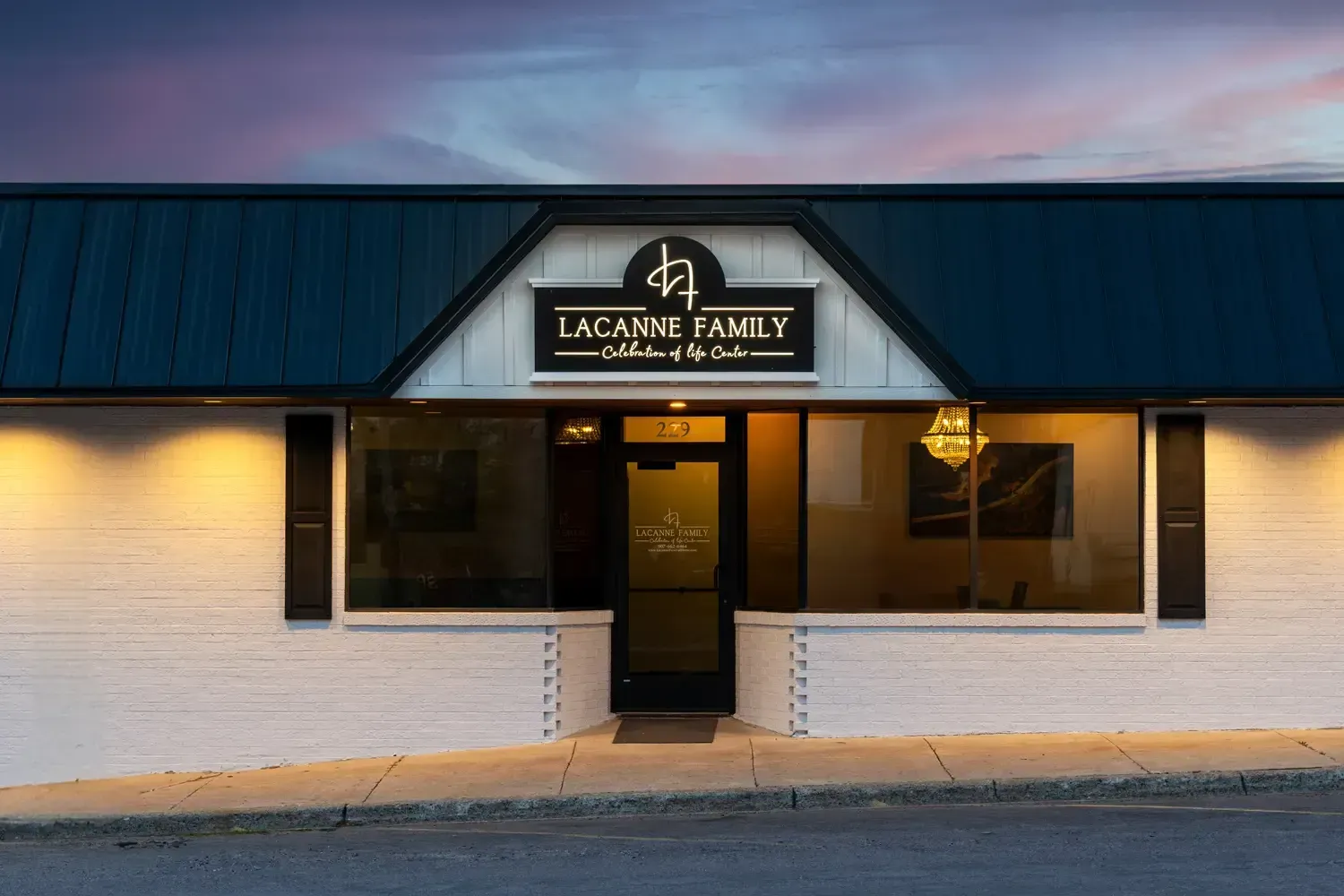 Exterior of a small storefront with a dark blue awning and lit entrance at dusk