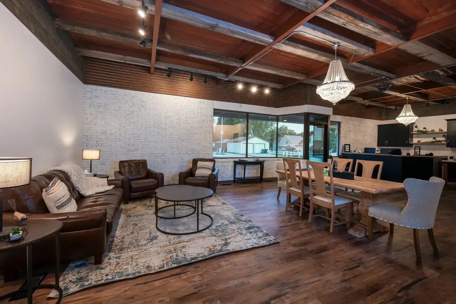 Spacious living-dining room with wood beam ceiling, chandelier, sofa, chairs, and large windows