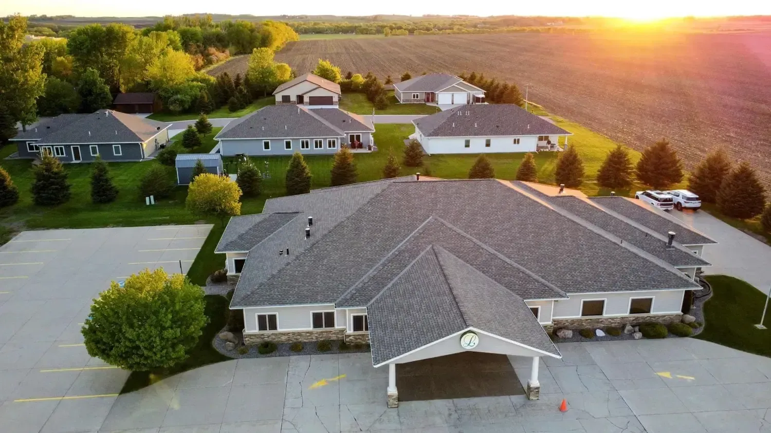 Aerial view of a large suburban house at sunset with surrounding homes and trees.