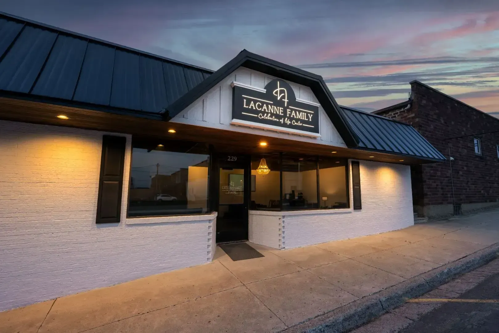 Exterior of a white storefront with a dark roof and lit windows at dusk, labeled “Legacy Parks” above the entrance