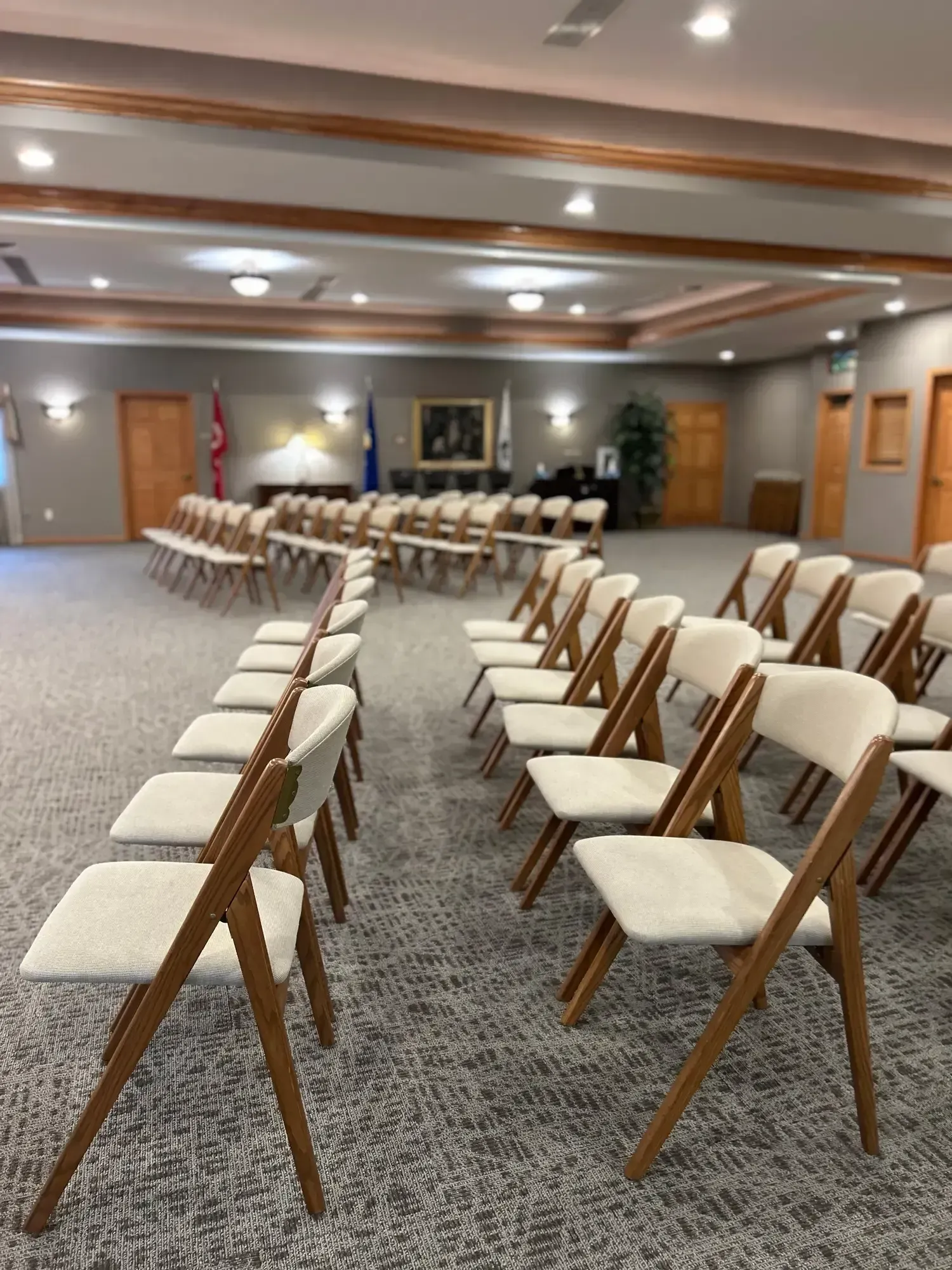 Empty conference room with rows of beige chairs facing a front wall and wood-trimmed ceiling lights