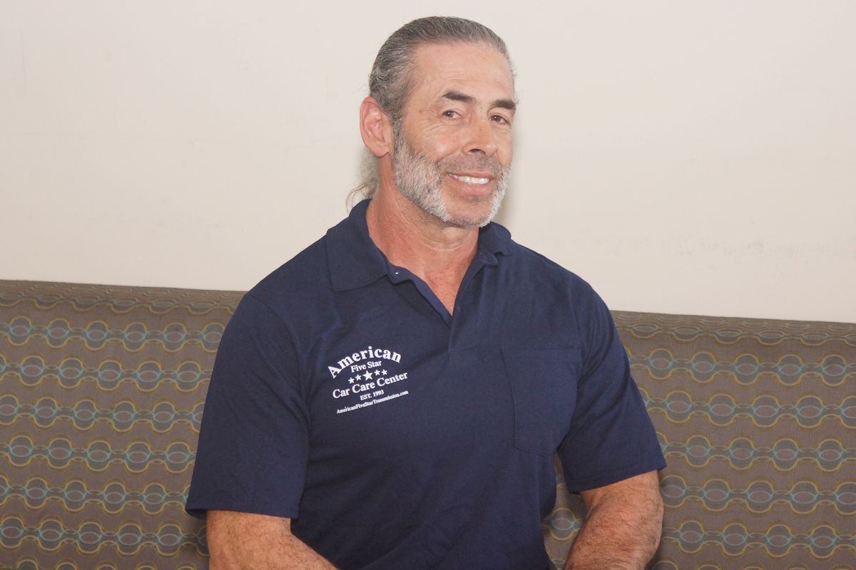 A man with a beard is sitting on a couch wearing a blue shirt.