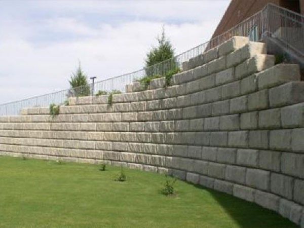 Large curved concrete block retaining wall supporting a sloped grassy area near a building as part of a concrete block retaining wall service in Heber City, UT