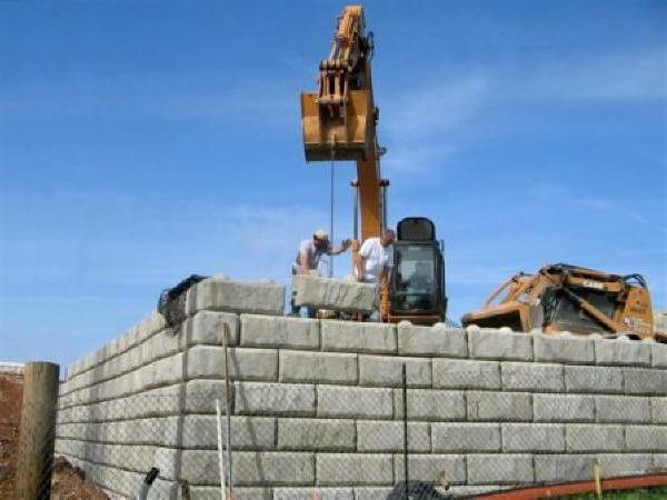 Crane lifting and placing large concrete blocks to form a tall retaining wall structure during a concrete block retaining wall service in Heber City, UT