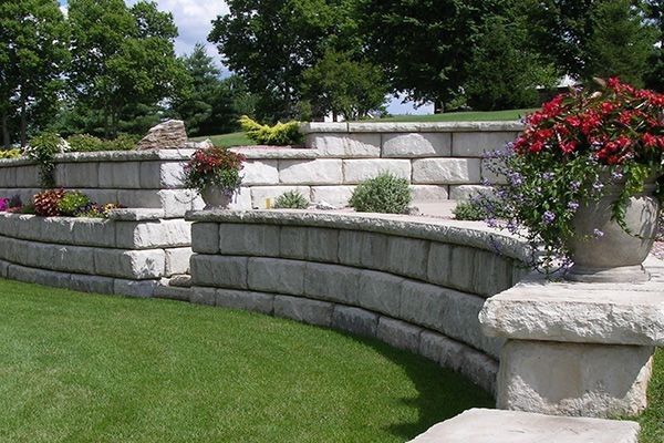 Decorative concrete block retaining wall with built-in planters and colorful flowers enhancing a landscaped yard during a concrete block retaining wall service in Heber City, UT