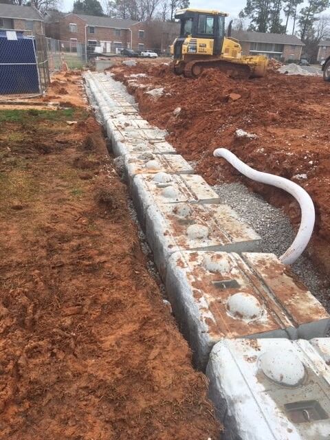 Construction crew preparing a gravel base and laying concrete blocks for a new retaining wall along a dirt site during a concrete block retaining wall service in Heber City, UT
