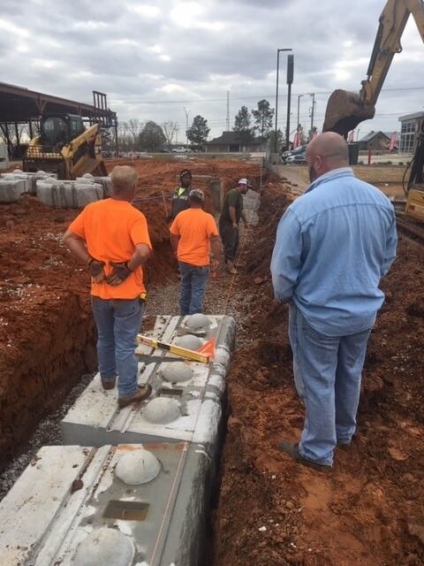 Workers and heavy equipment excavating soil and preparing the ground for a retaining wall build during a concrete block retaining wall service in Heber City, UT