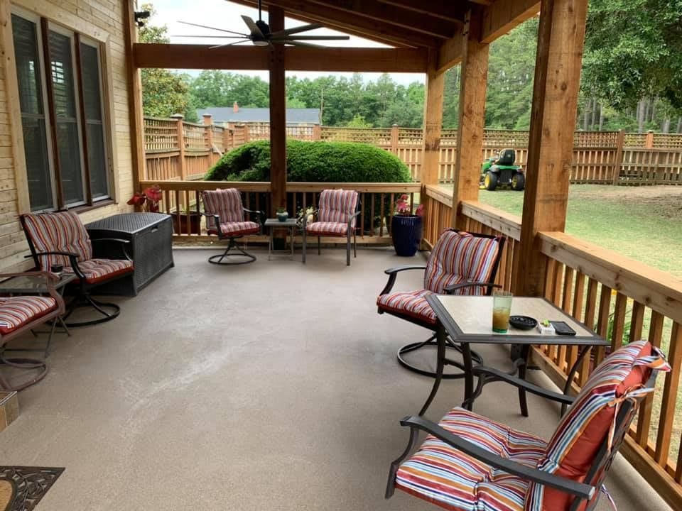 Covered patio with seating, view of backyard, brown wooden railings and supports.