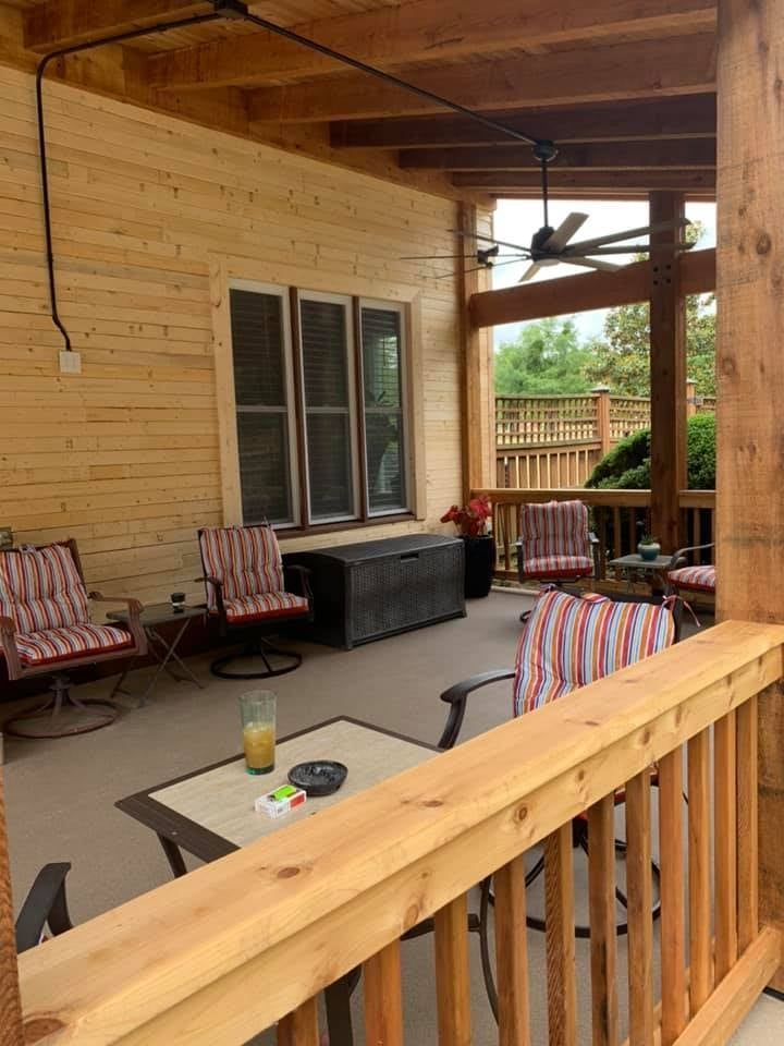 Covered patio with seating, wooden features, and a view of a backyard.