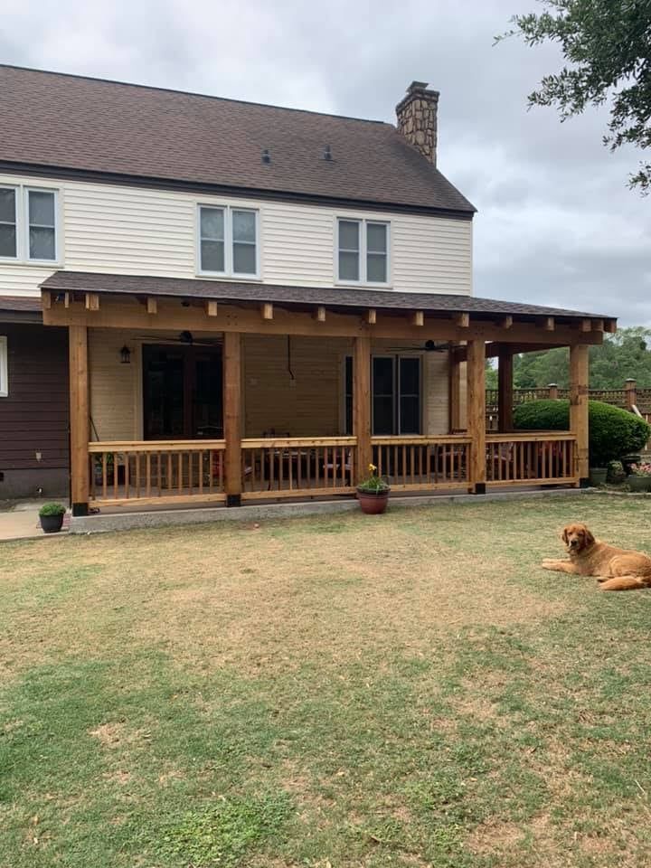 A large wooden covered patio attached to a house, with a dog lying in the grass.