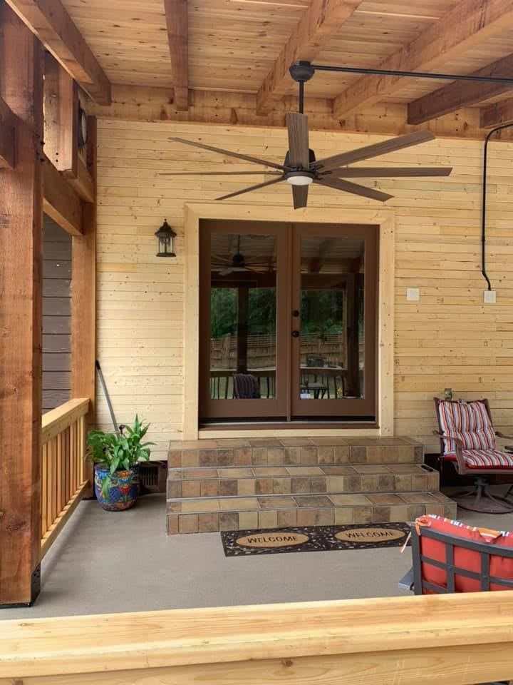 Covered porch with wood ceiling, steps, brown doors, and a large ceiling fan.