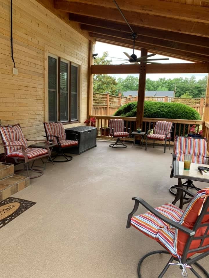Covered porch with seating and wooden beams overlooking a yard.