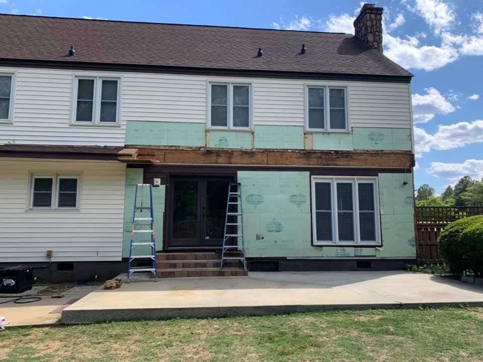 Back of a house under construction: green insulation, ladders, and a concrete patio.