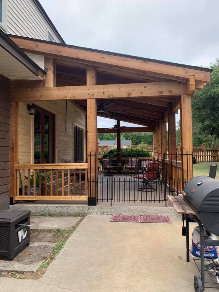 A wooden patio cover extends from a house, featuring a small fence and a grill outside.