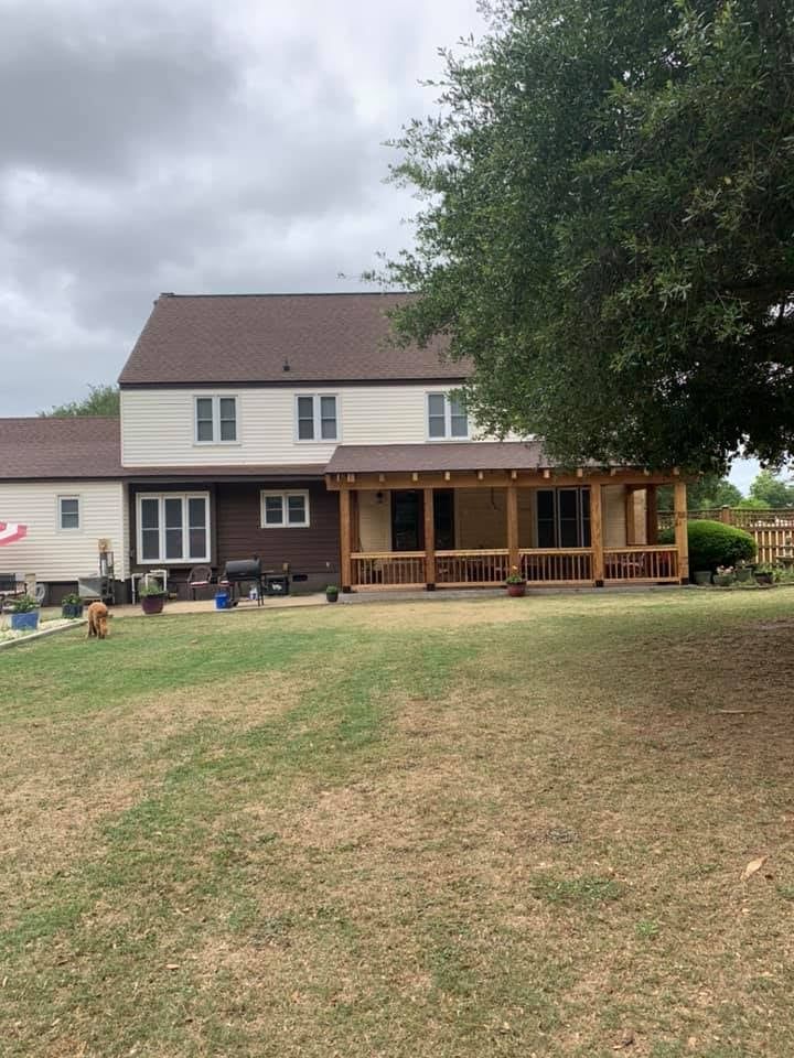 Backyard view of a two-story house with a brown porch, grassy lawn, and an overcast sky.
