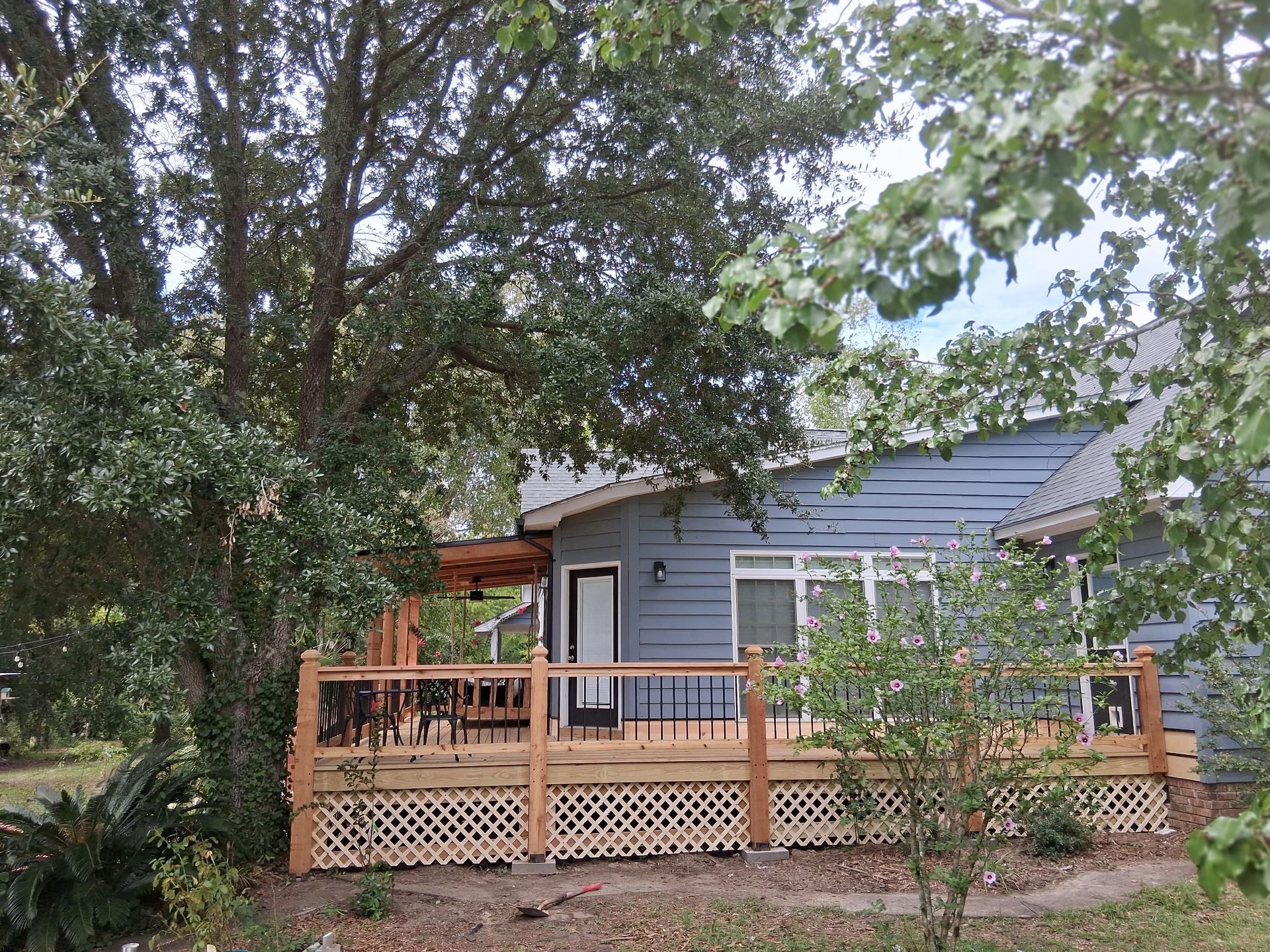 Blue house with wooden deck, surrounded by trees.