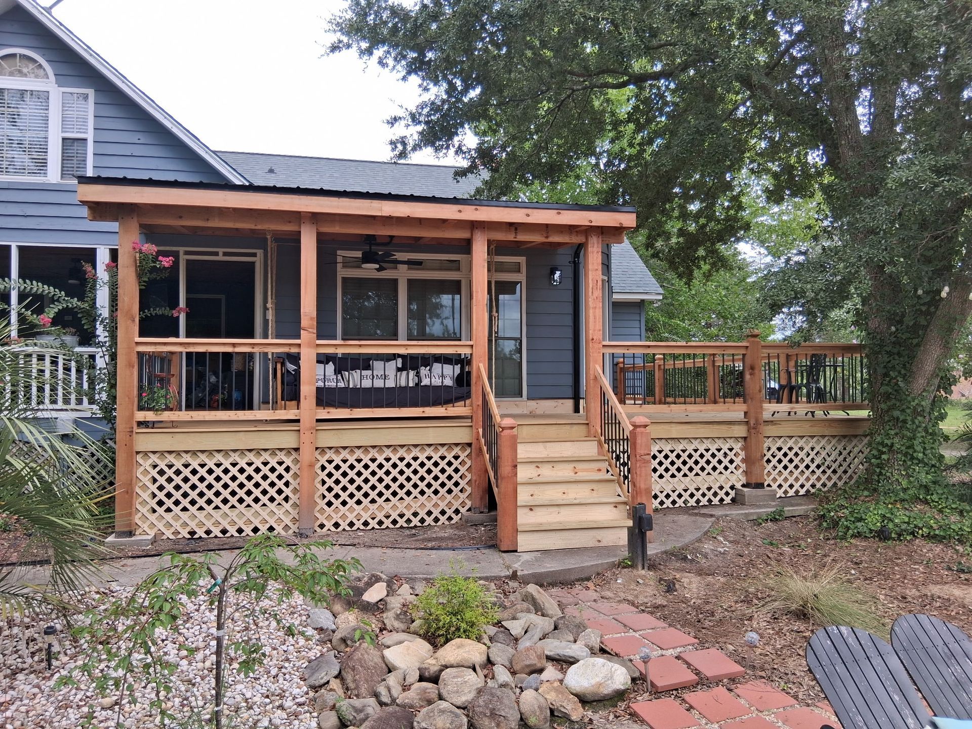 Wooden deck with lattice skirting, stairs to a covered porch and a blue house.
