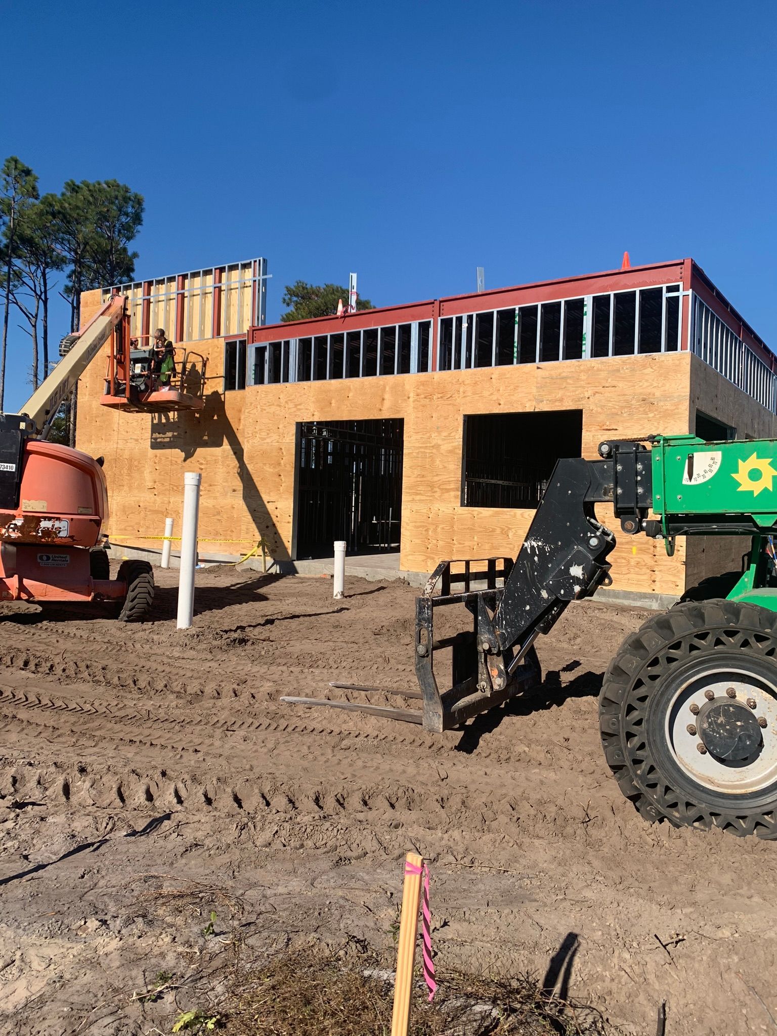 Construction site with workers, lift, and heavy machinery. Building's frame is up, sunny day.