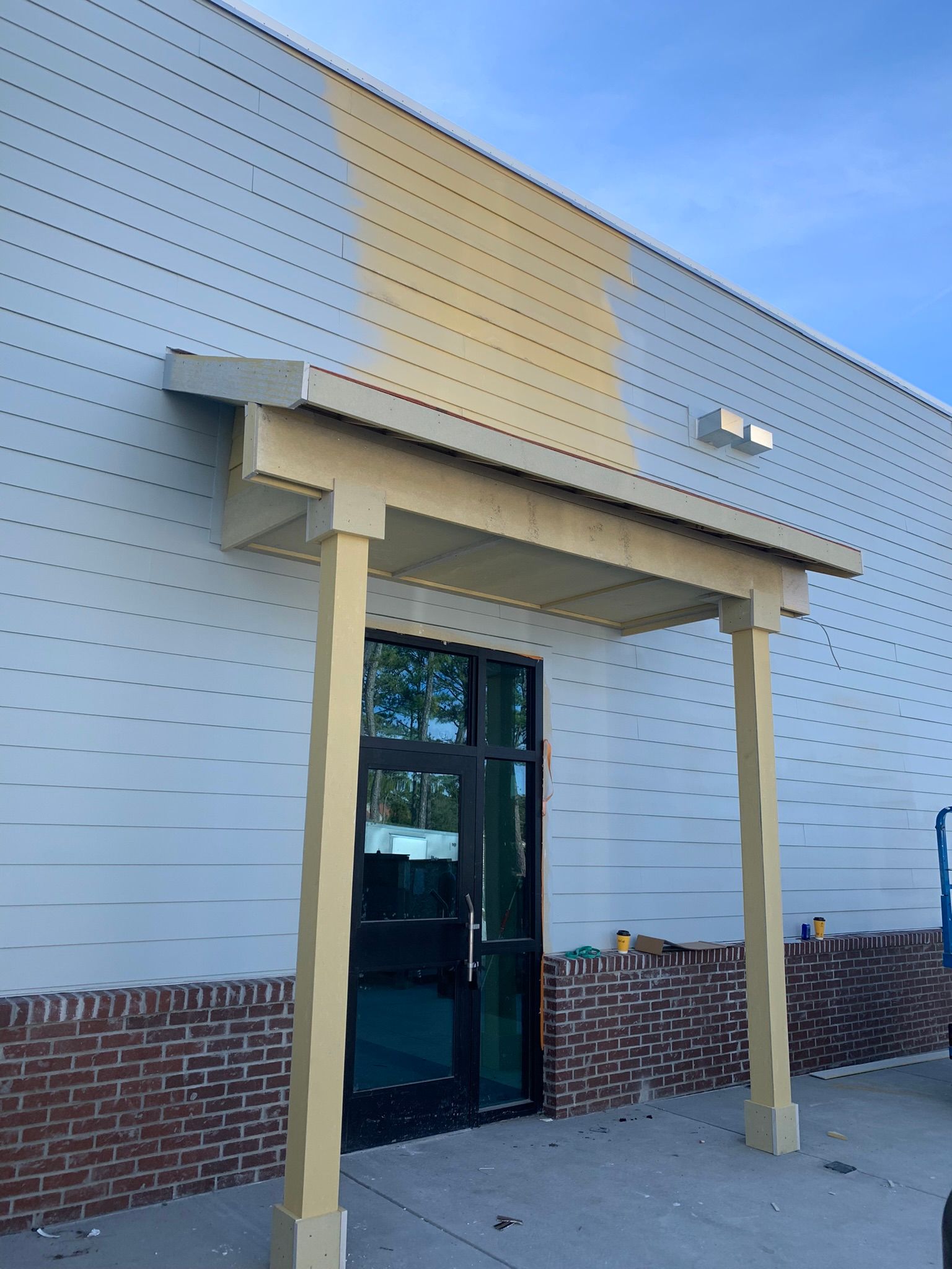 Entrance with tan awning and columns, black door, brick base, light blue building.