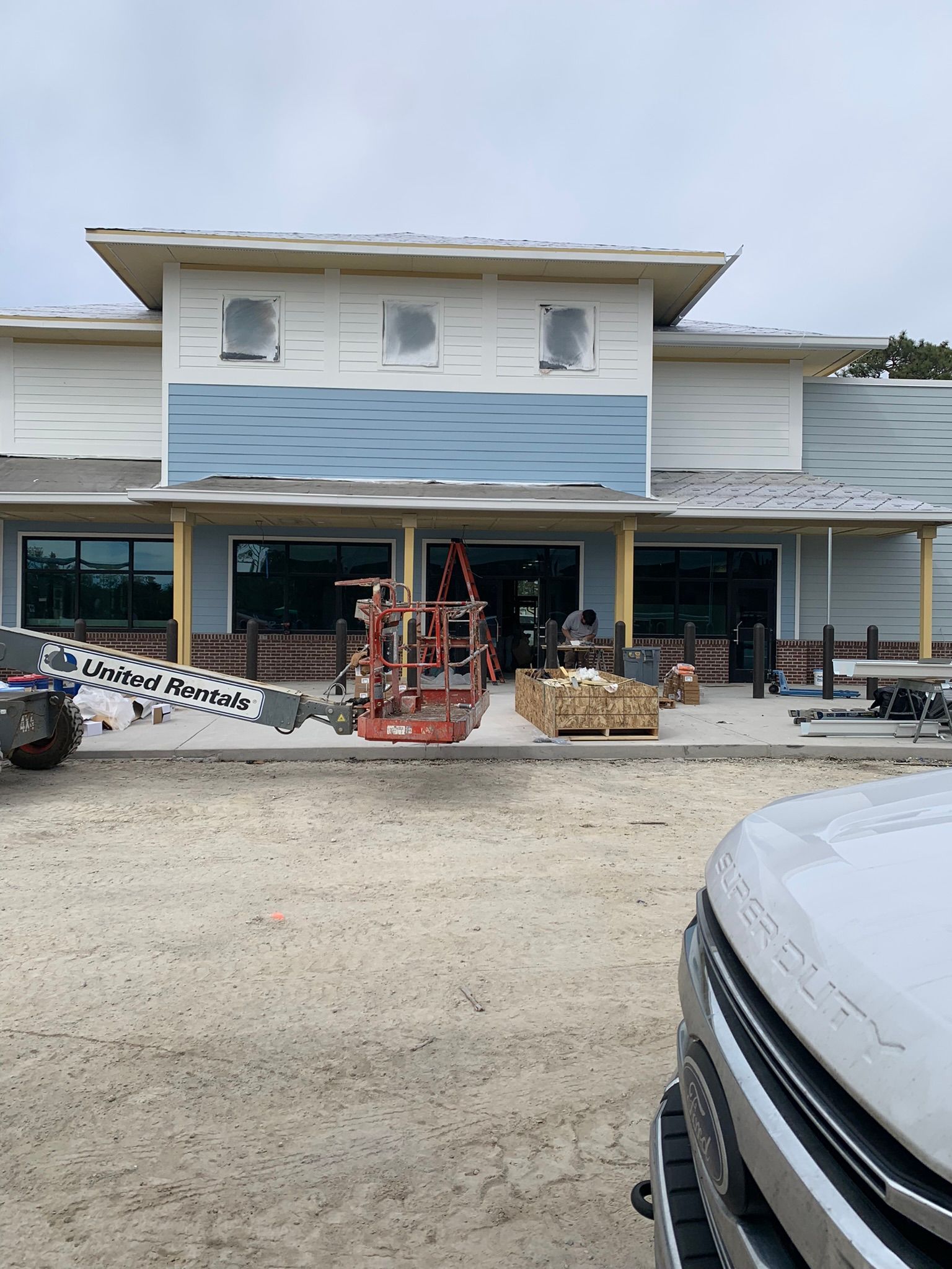 Construction site of a building with blue siding, windows, and a lift.