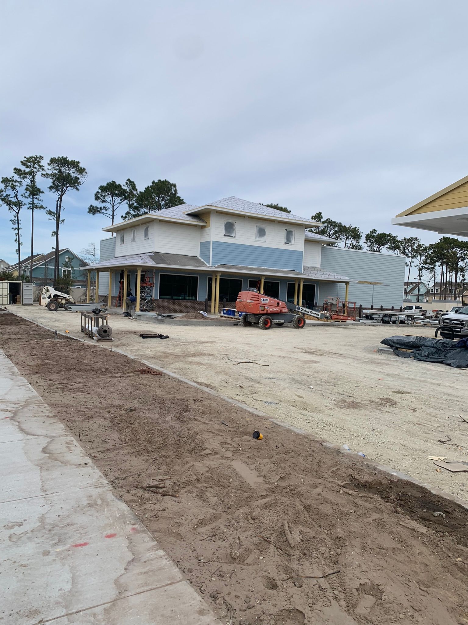 Building under construction in a sandy lot, with a cloudy sky overhead.