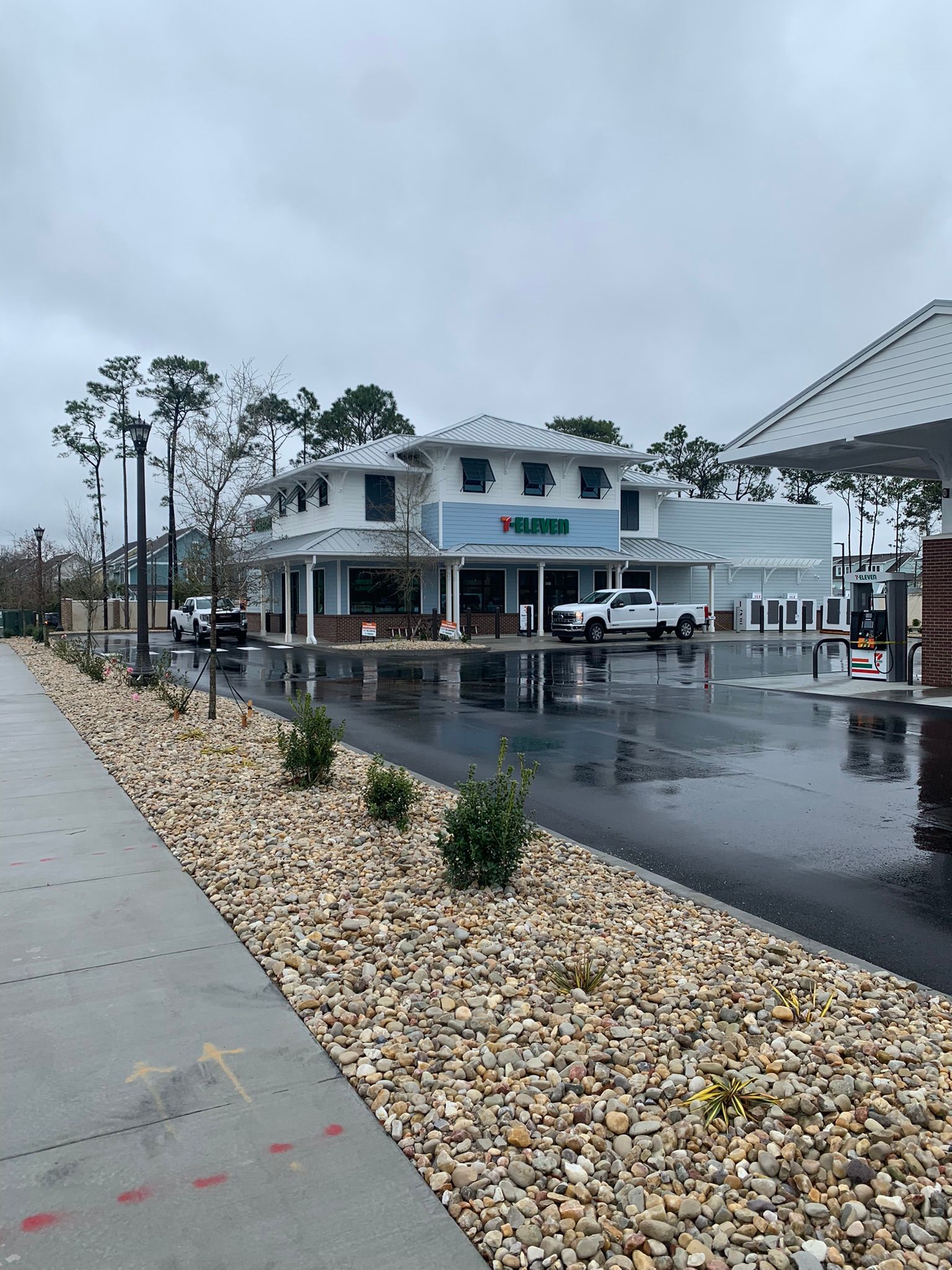 Exterior view of a building on a wet, gray day. Two white trucks parked in front of the building with bushes and river rock.