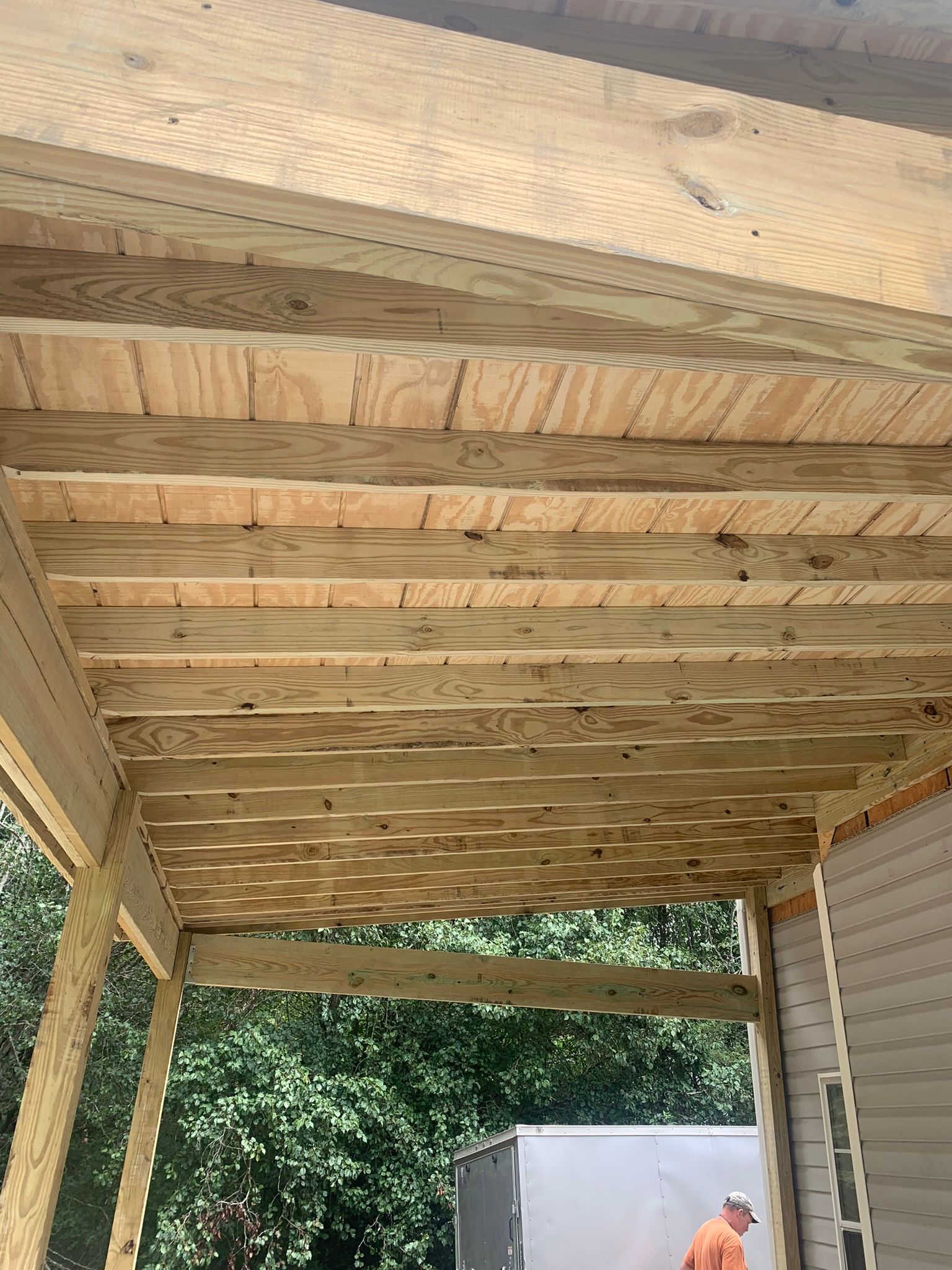 Wooden porch ceiling under construction with a person in the background.