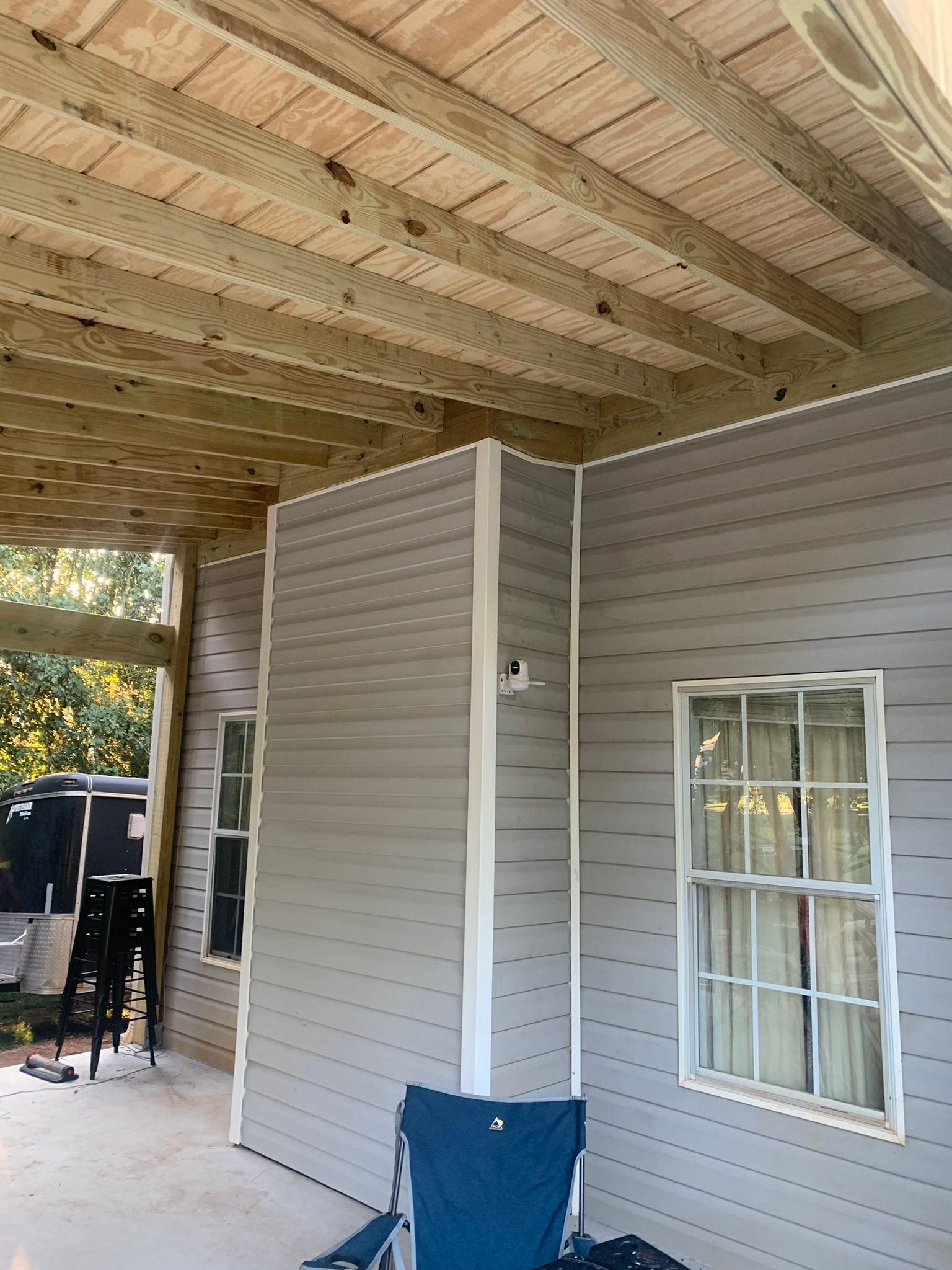 Outdoor structure with gray siding, white trim, and a wooden ceiling. A blue chair is in the foreground.