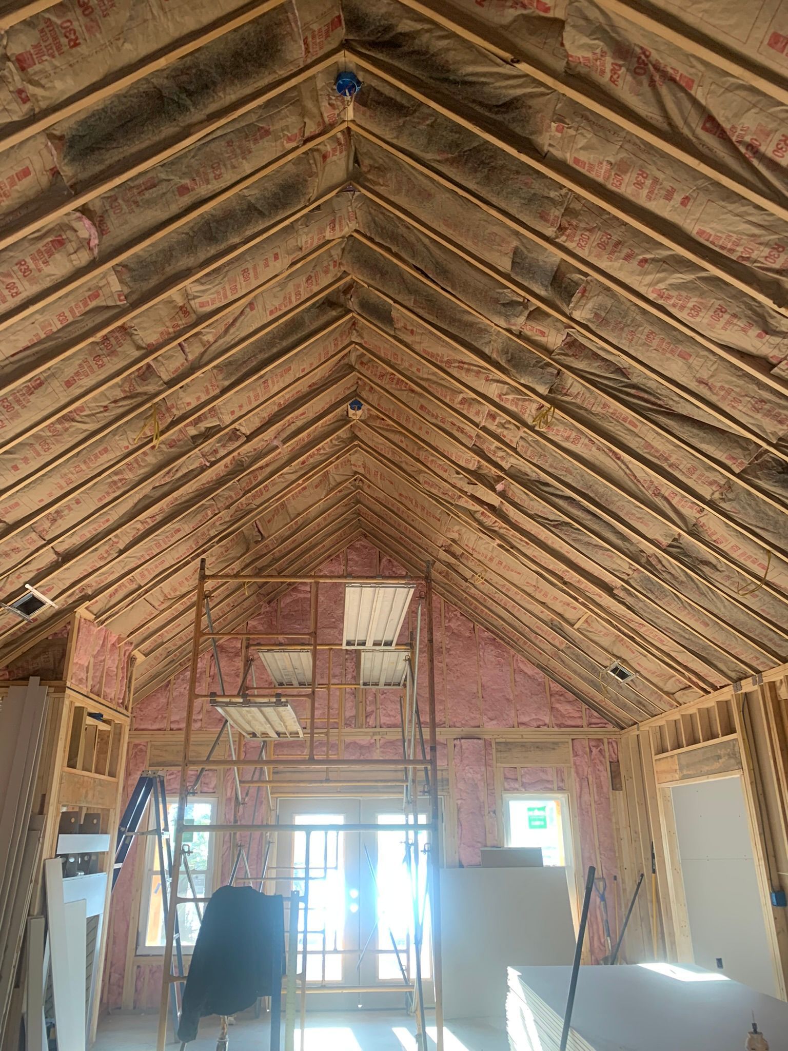 Interior framing of a house under construction, showing the roof beams, insulation, and a scaffold.