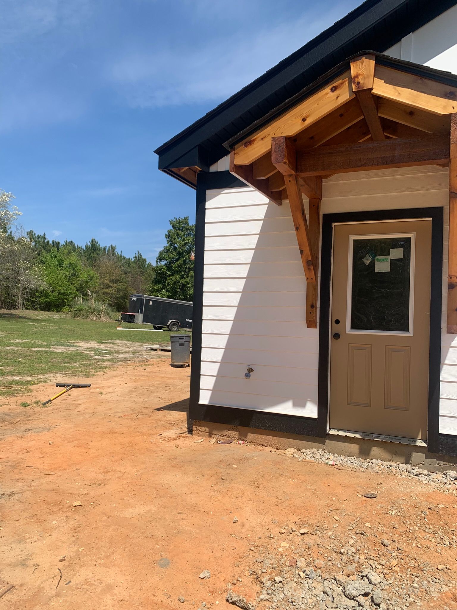 White house with a brown door and wooden awning, set on a red dirt yard.