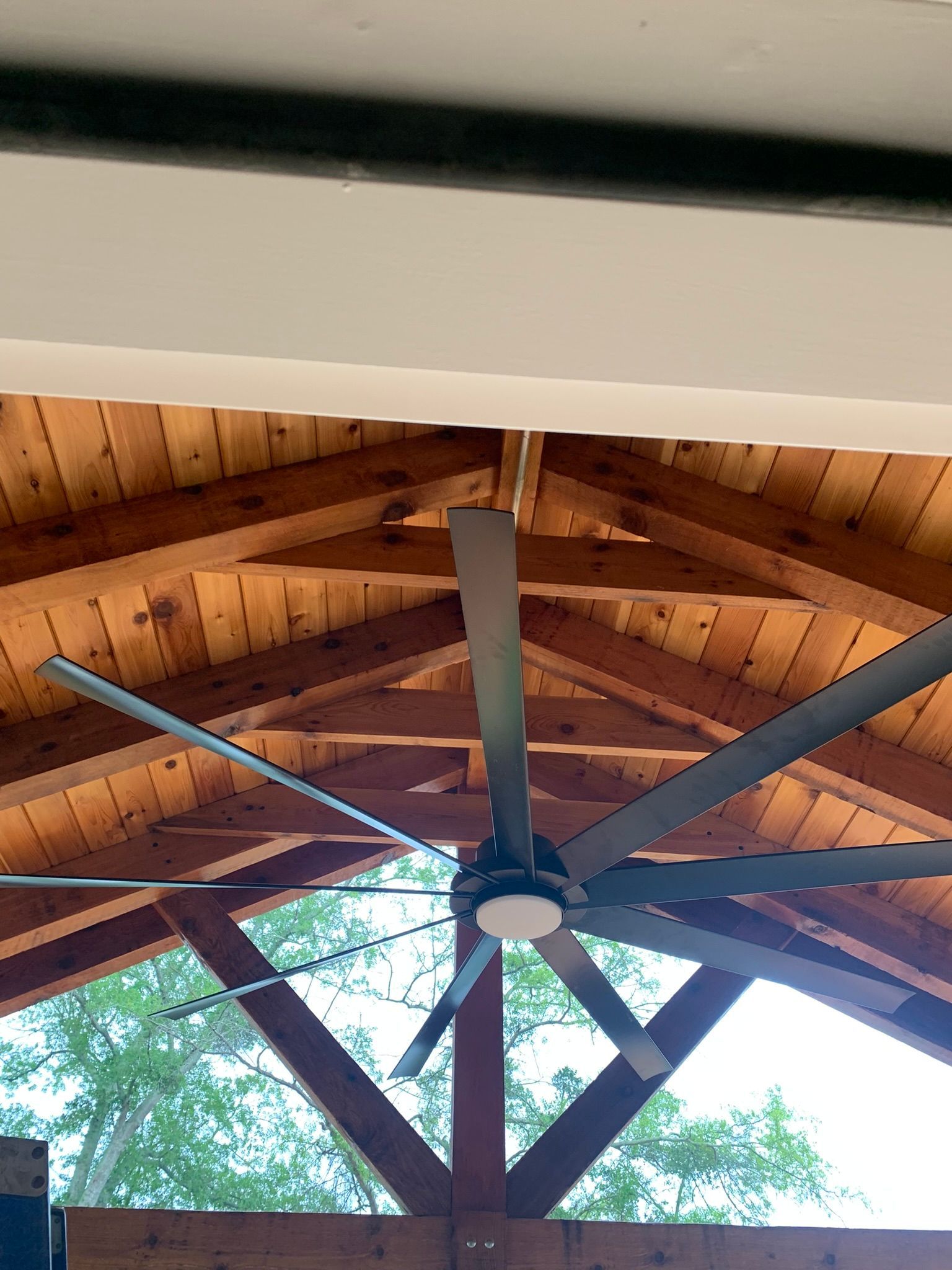 A large ceiling fan with gray blades hangs from a wooden, peaked roof.