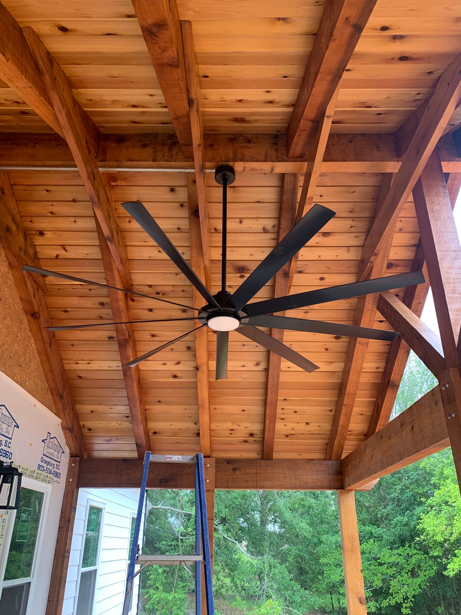 Black ceiling fan hangs from a wooden porch ceiling. Ladder visible.