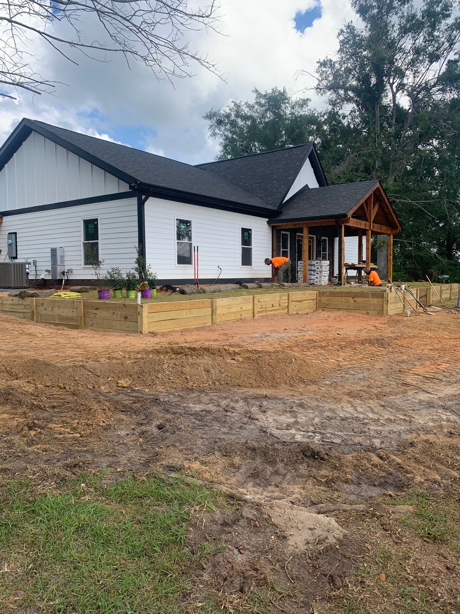 White house with black trim and porch. Raised wooden garden beds in front. Dirt yard.