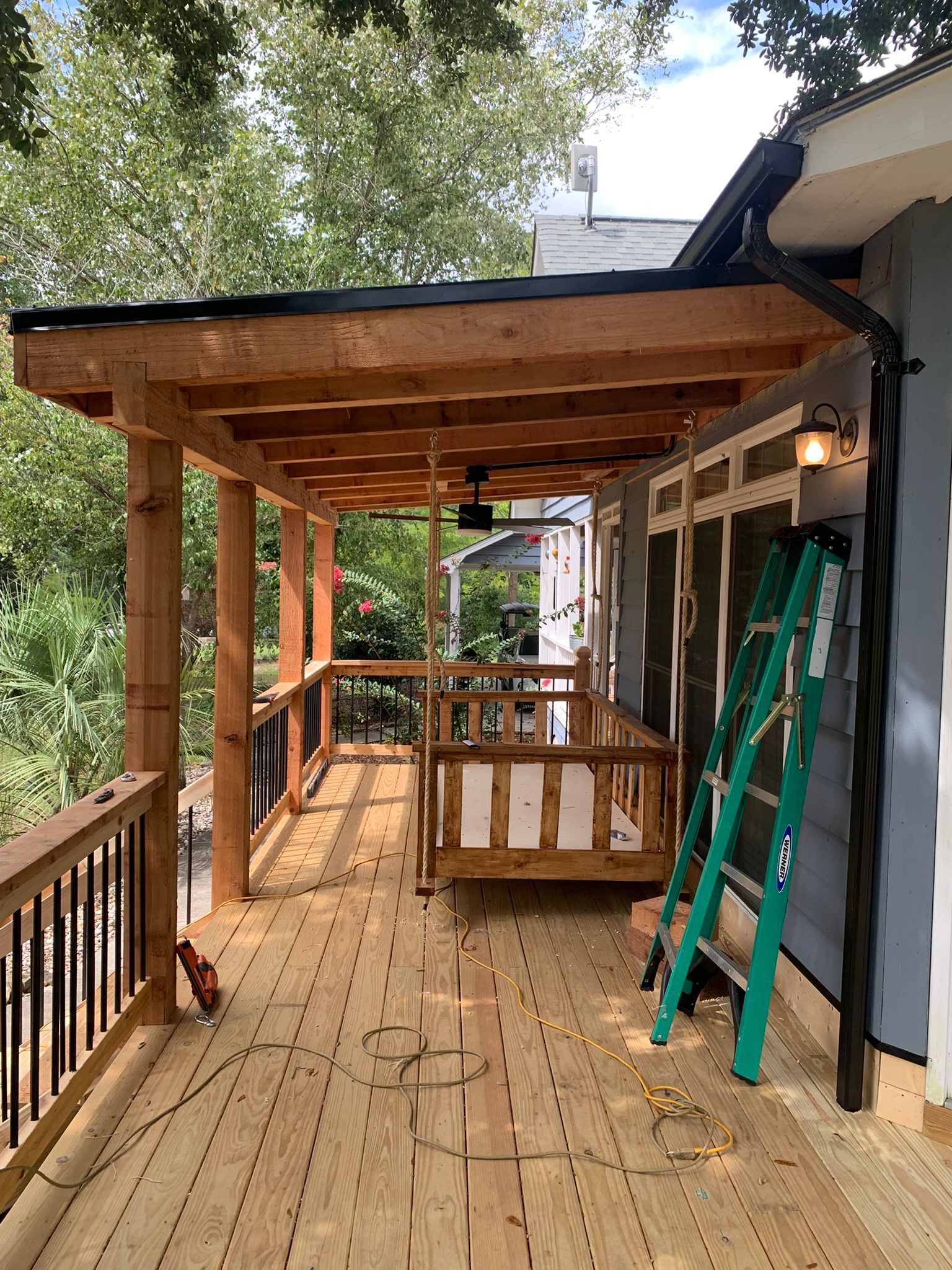 Wooden deck with a canopy and a swing, under construction. A ladder leans against the house.