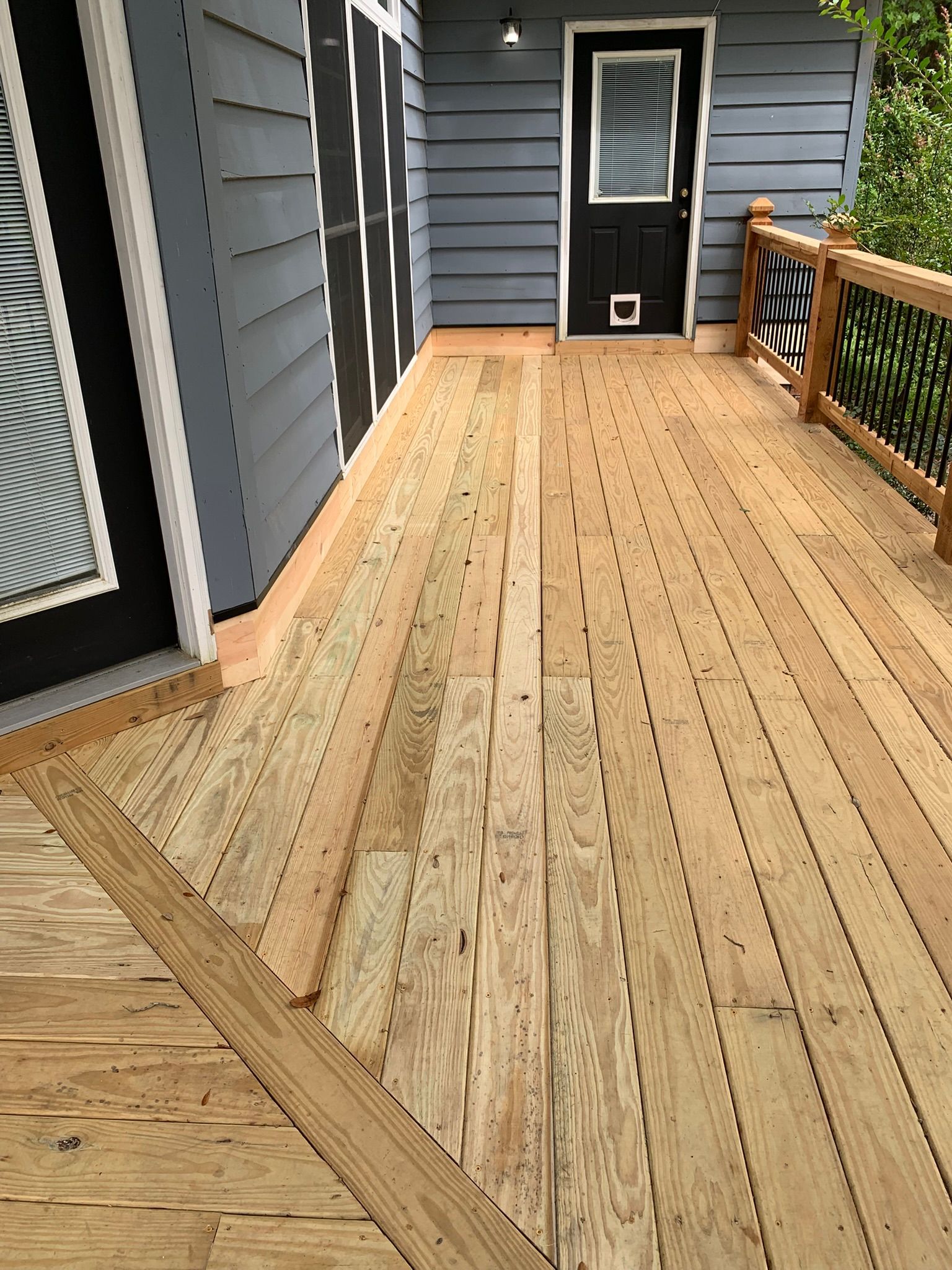 Wood deck with gray house siding, black door, and wooden railing.